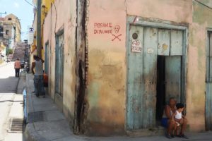 Woman with a little boy sitting in front of a house with a warning sign in Santiago de Cuba.